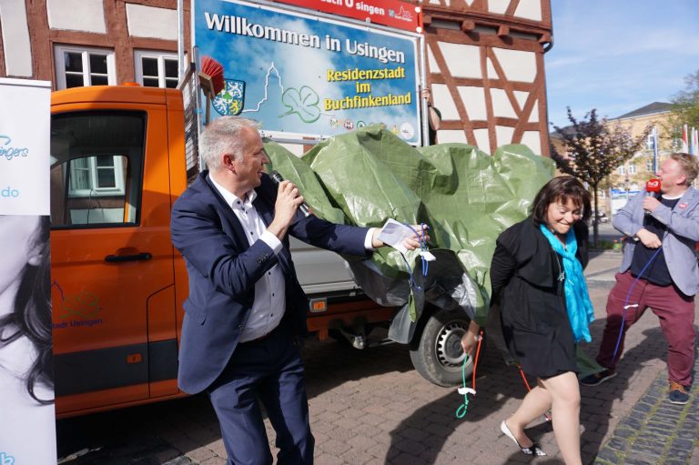 Glückliche Schild-Enthüller (v.l.n.r.): Bürgermeister Steffen Wernard, Chorleiterin Anja Fiethen und Moderator Jonas Schulte enthüllen das Schild mit dem Slogan.