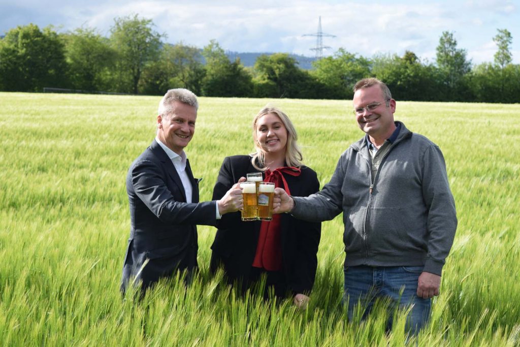 Die designierte Laternenkönigin Johanna I. stößt mit Dr. Jochen Habetha (li.) und Landwirt Stefan Wagner mitten im Weizenfeld an. - Foto: Privat